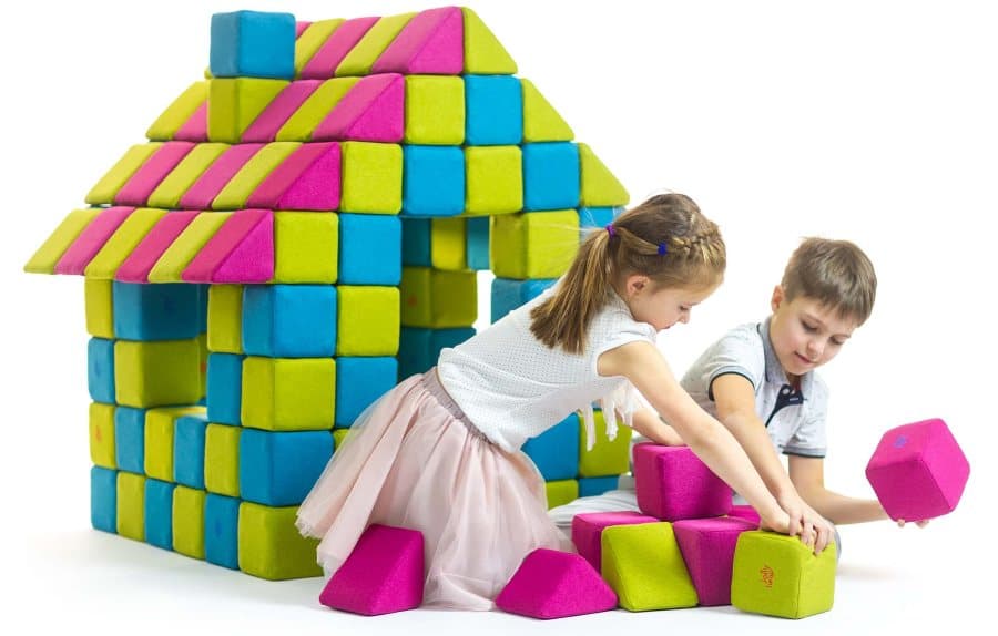 A girl and a boy adding pink and green JollyHeap blocks in front of a block house