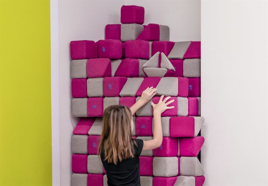 A girl adding a block to a tall wall built from pink and grey JollyHeap blocks