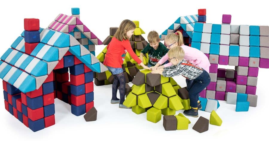 Four children building a mound of JollyHeap blocks together between two block houses