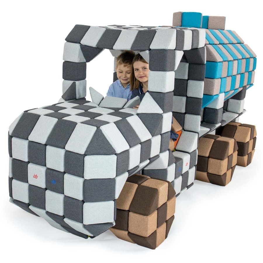 Two children sitting in the cab of a lorry built entirely from grey JollyHeap blocks