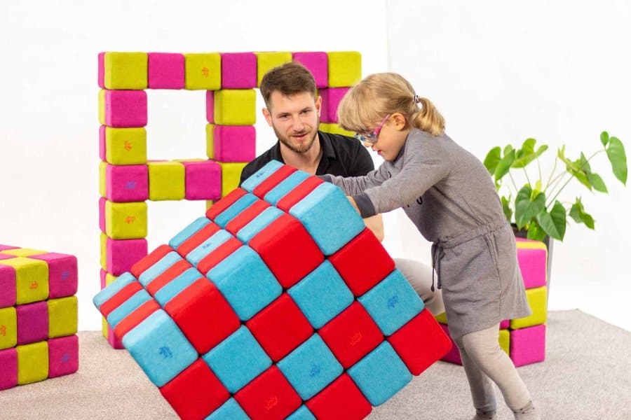A therapist and a girl in glasses turning a large cube of red and blue JollyHeap blocks together