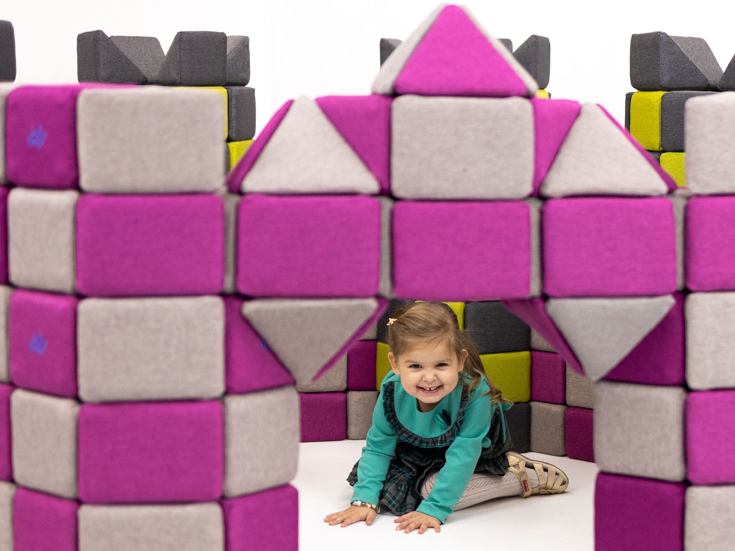A girl crawls out through the gate of a pink and grey castle built from JollyHeap blocks