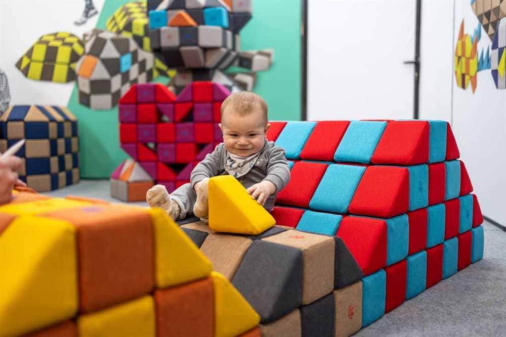 A baby sitting on blocks and grabbing a yellow triangular block