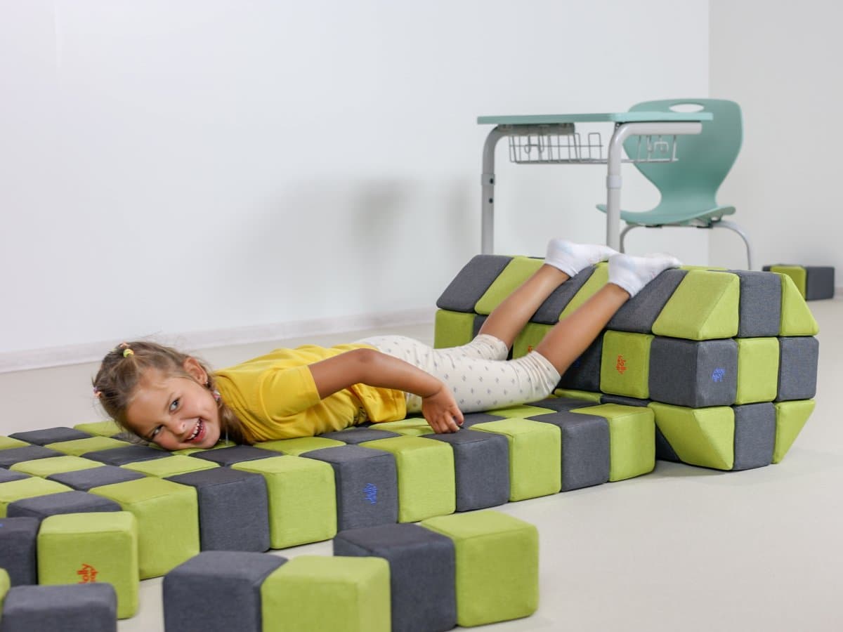 A smiling girl lying on a roller made of soft blocks