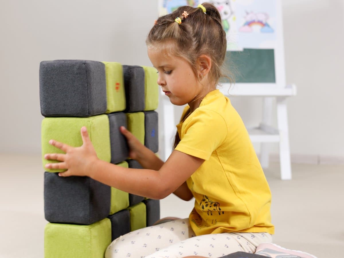 A girl building a wall from green and grey blocks