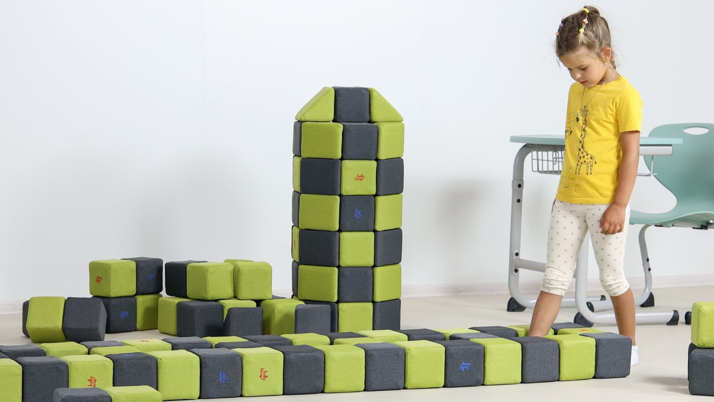 A girl walking along a path of soft magnetic blocks next to a block tower