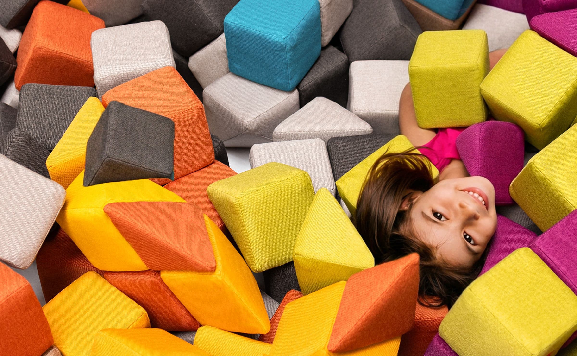 A girl lying and laughing in a heap of colourful JollyHeap blocks