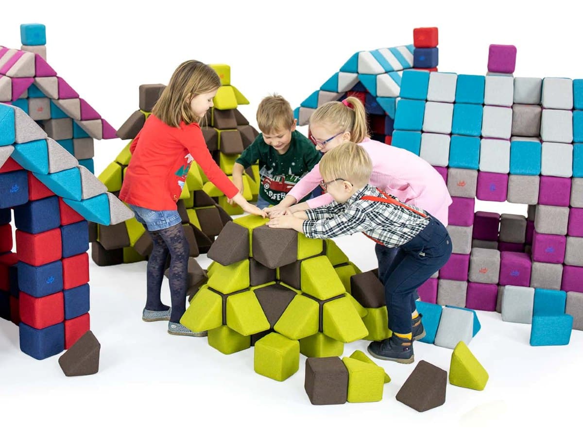 Four children building a structure together from JollyHeap blocks, with block-built houses behind them