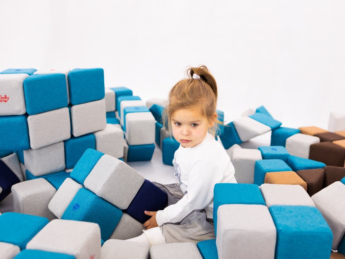 A toddler playing on her own among blue and grey JollyHeap blocks spread across the floor