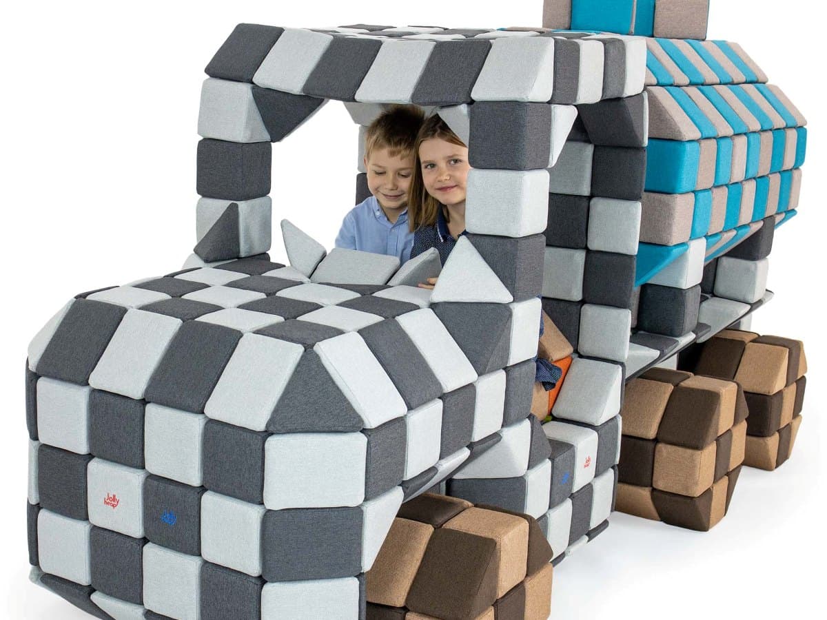 Two children sitting in the cab of a huge truck built entirely from grey JollyHeap blocks