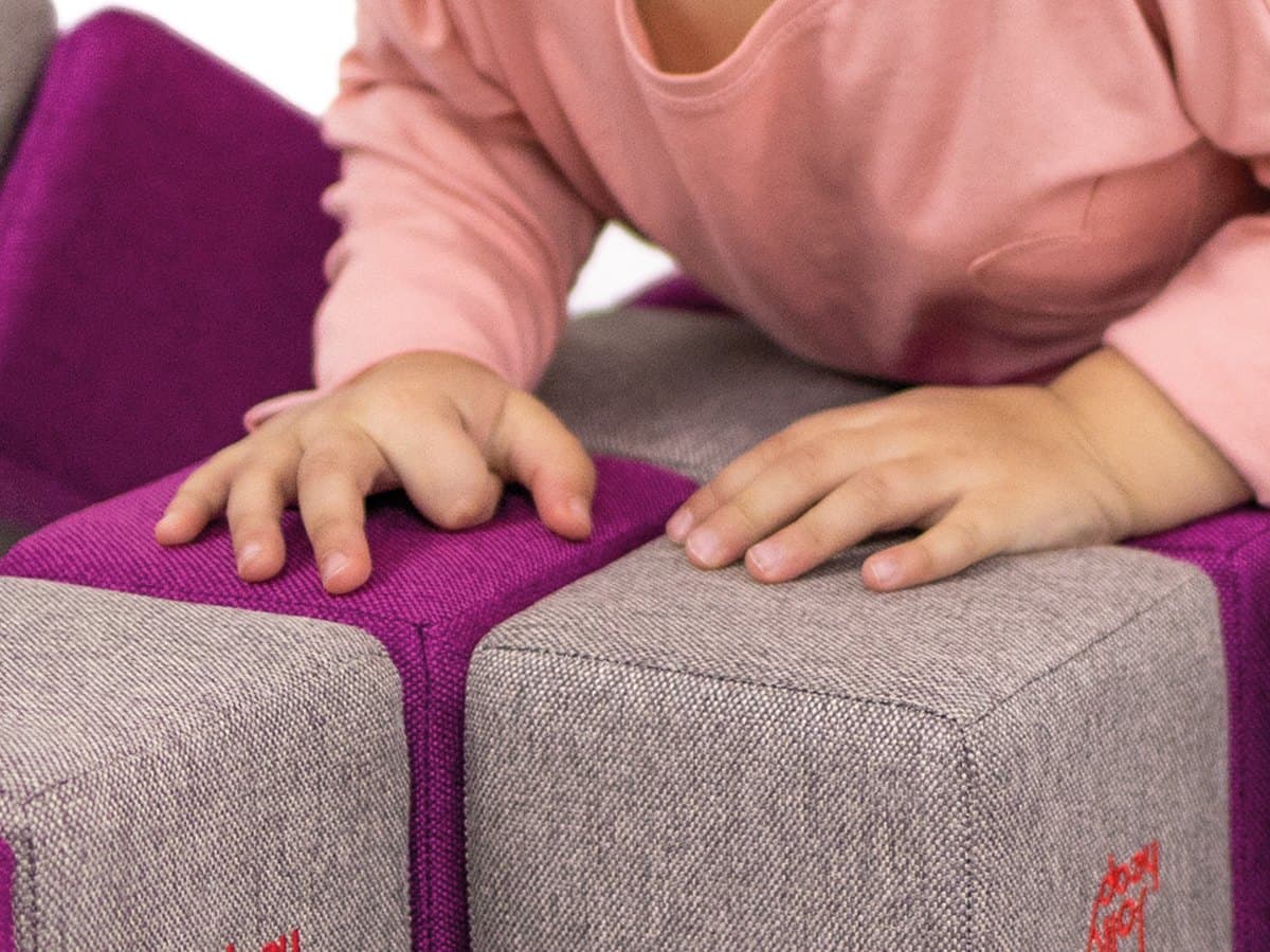 Close-up of a child hands on the woven fabric of two JollyHeap blocks, purple and grey