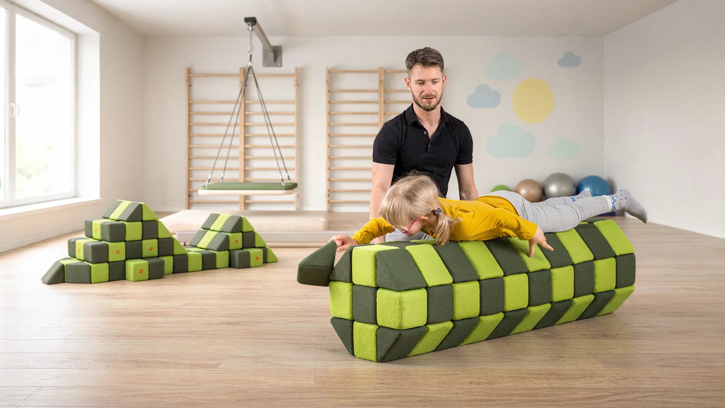 A therapist supporting a girl lying face down on a long roller built from green JollyHeap blocks in a therapy room