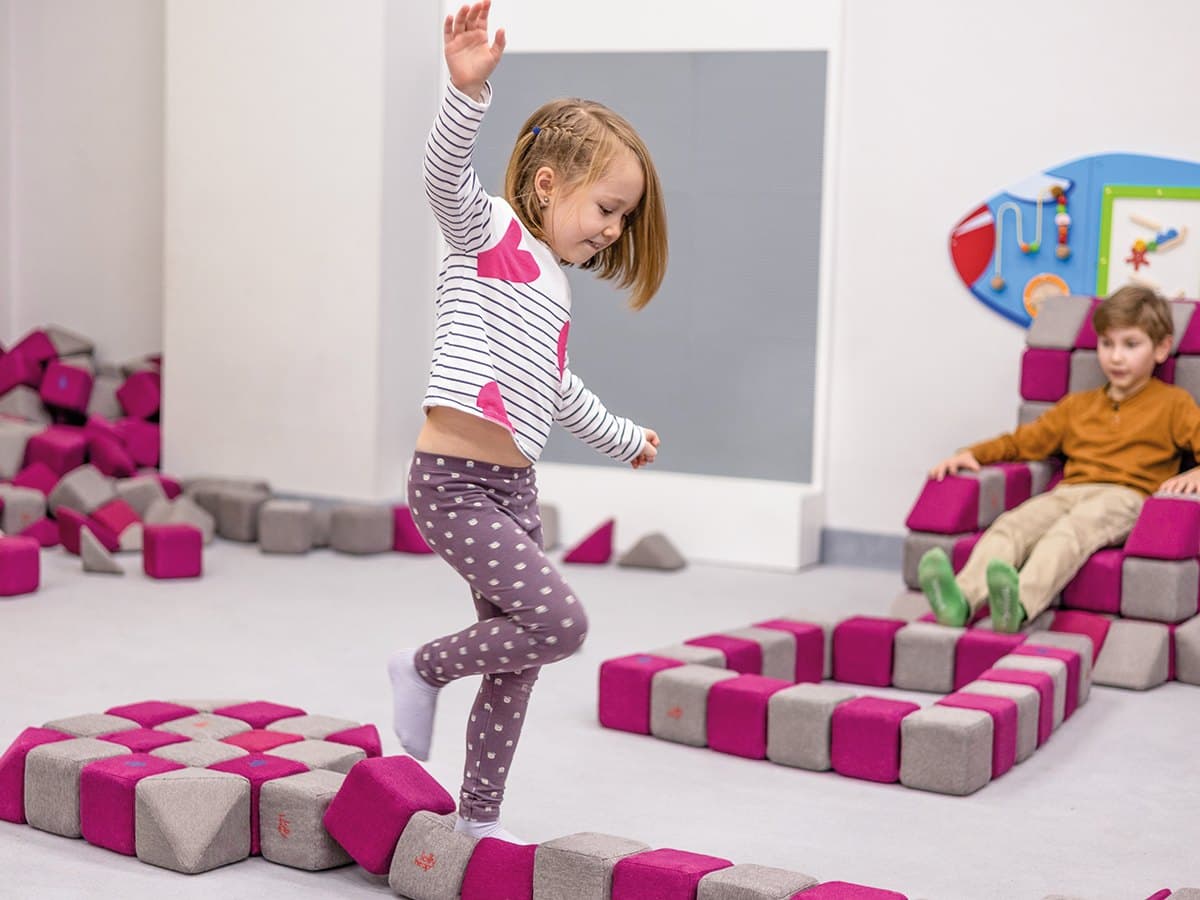 A girl with one arm raised walking along a balance path made of pink and grey JollyHeap blocks