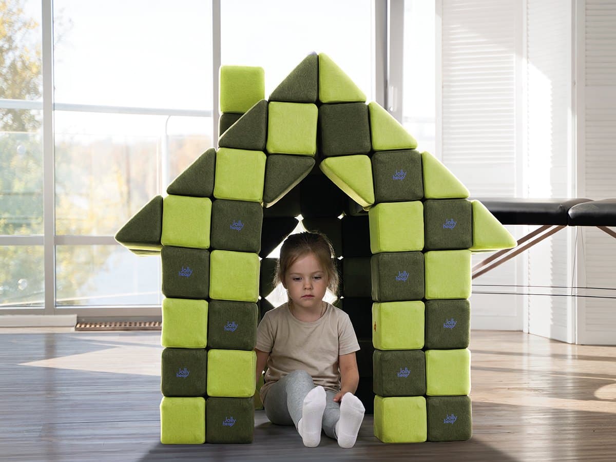 A girl sitting inside a house with a pitched roof built from green JollyHeap blocks in a bright room